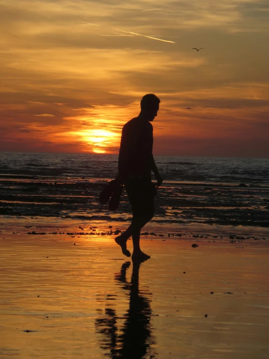 man walking on beach at sunset near ocean