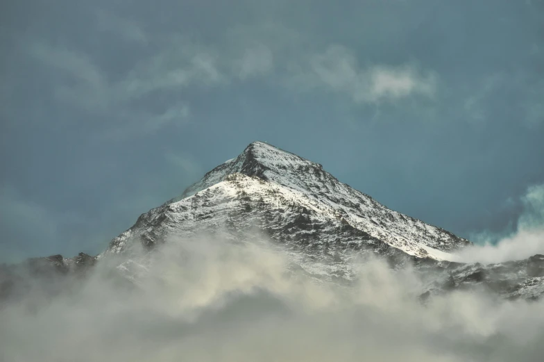 a snowy mountain peaks above clouds as the sun goes down