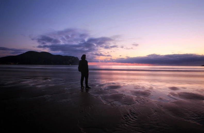 a person stands on a beach with the sun setting in the background