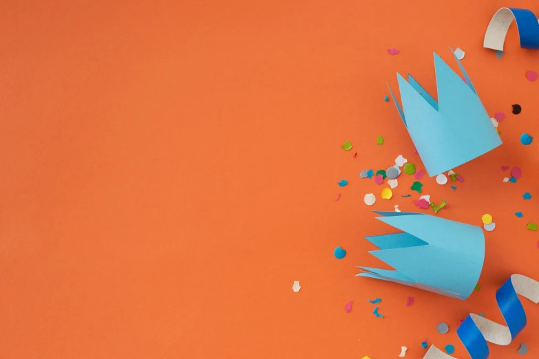 one paper hat with colorful streamers and confetti on an orange background