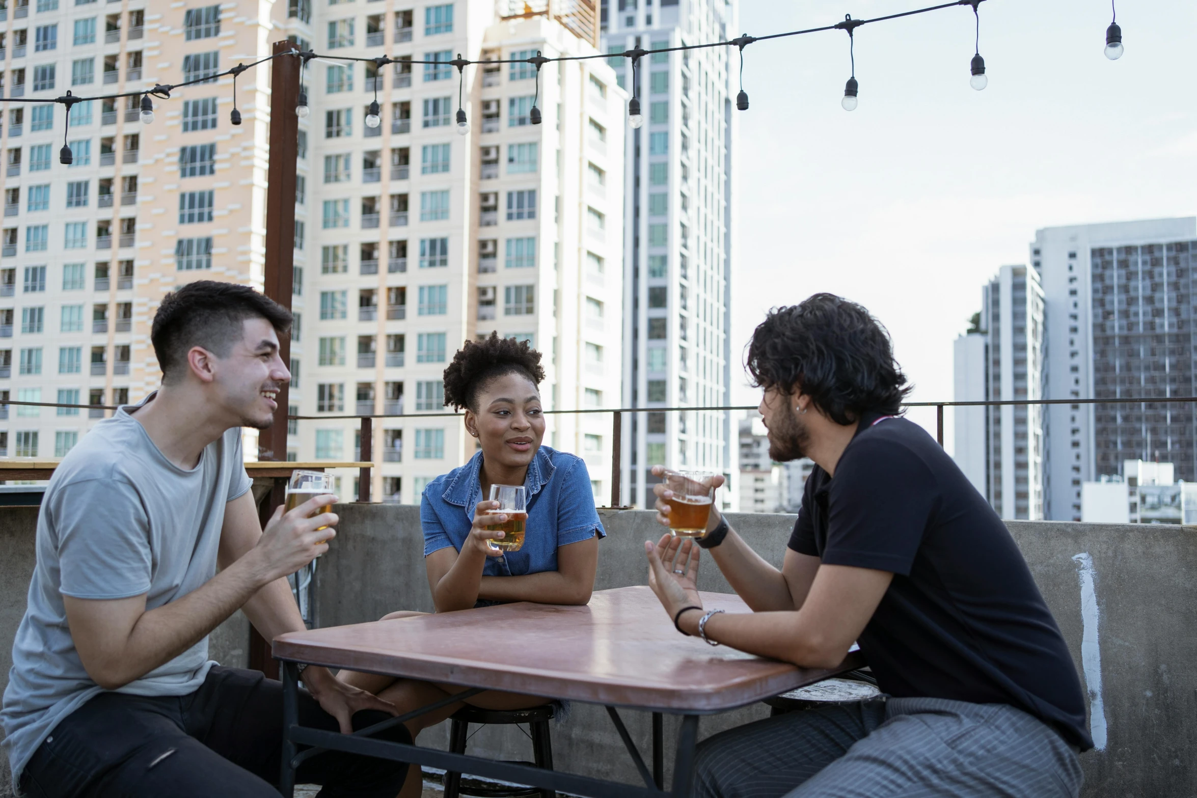 three friends toasting beers on a city rooftop