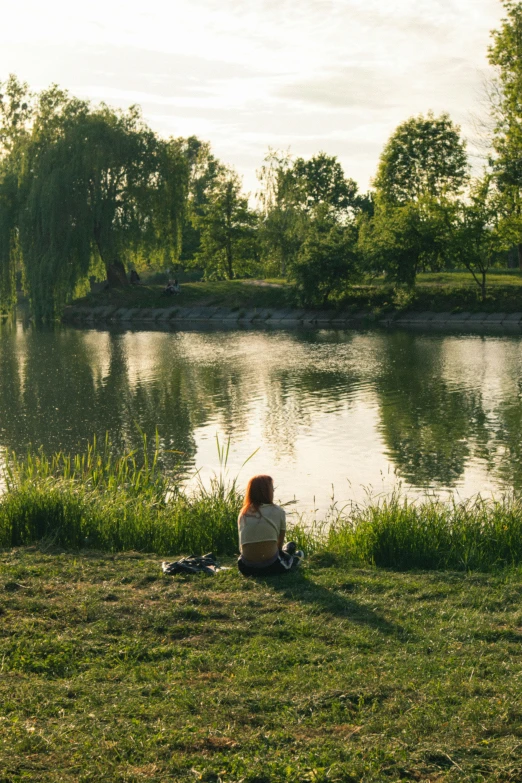 a woman sitting on the grass looking out over water