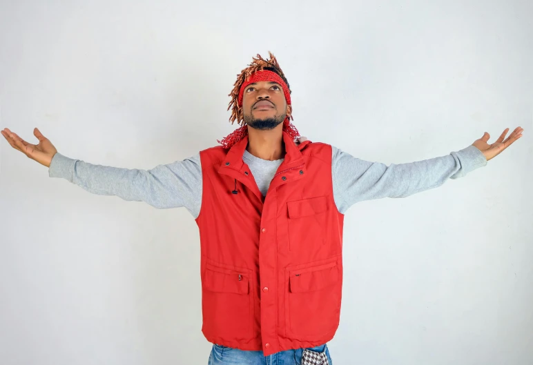 a man in a red vest and bandana stands with his arms spread out