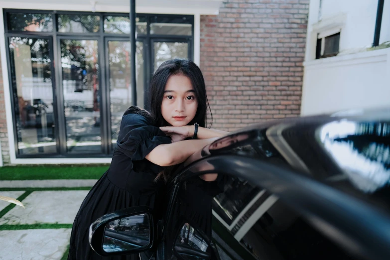 a person leaning on a black car in front of a brick building