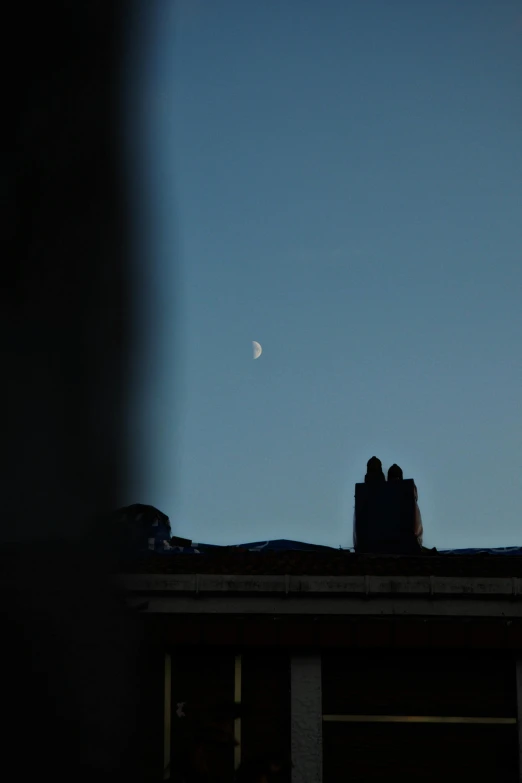 the moon is visible over a couple of buildings