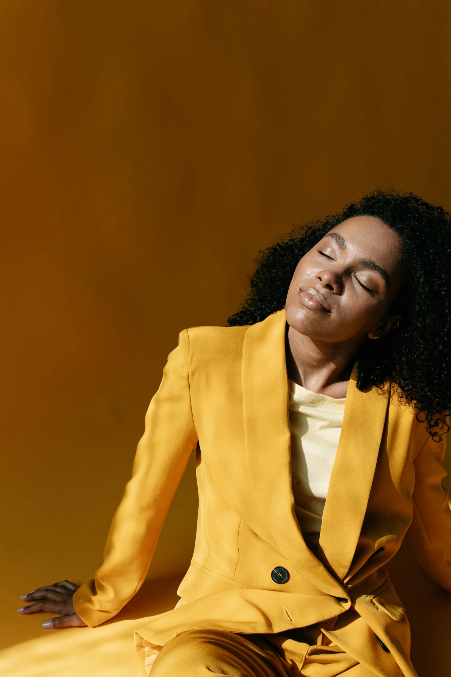 a woman wearing a bright yellow suit and sitting in the middle of a floor