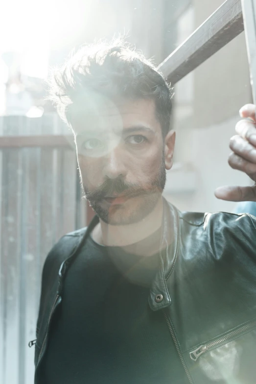 a man wearing a black leather jacket standing by a window