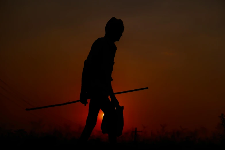 a silhouetted person with a bag standing with the sun setting behind them