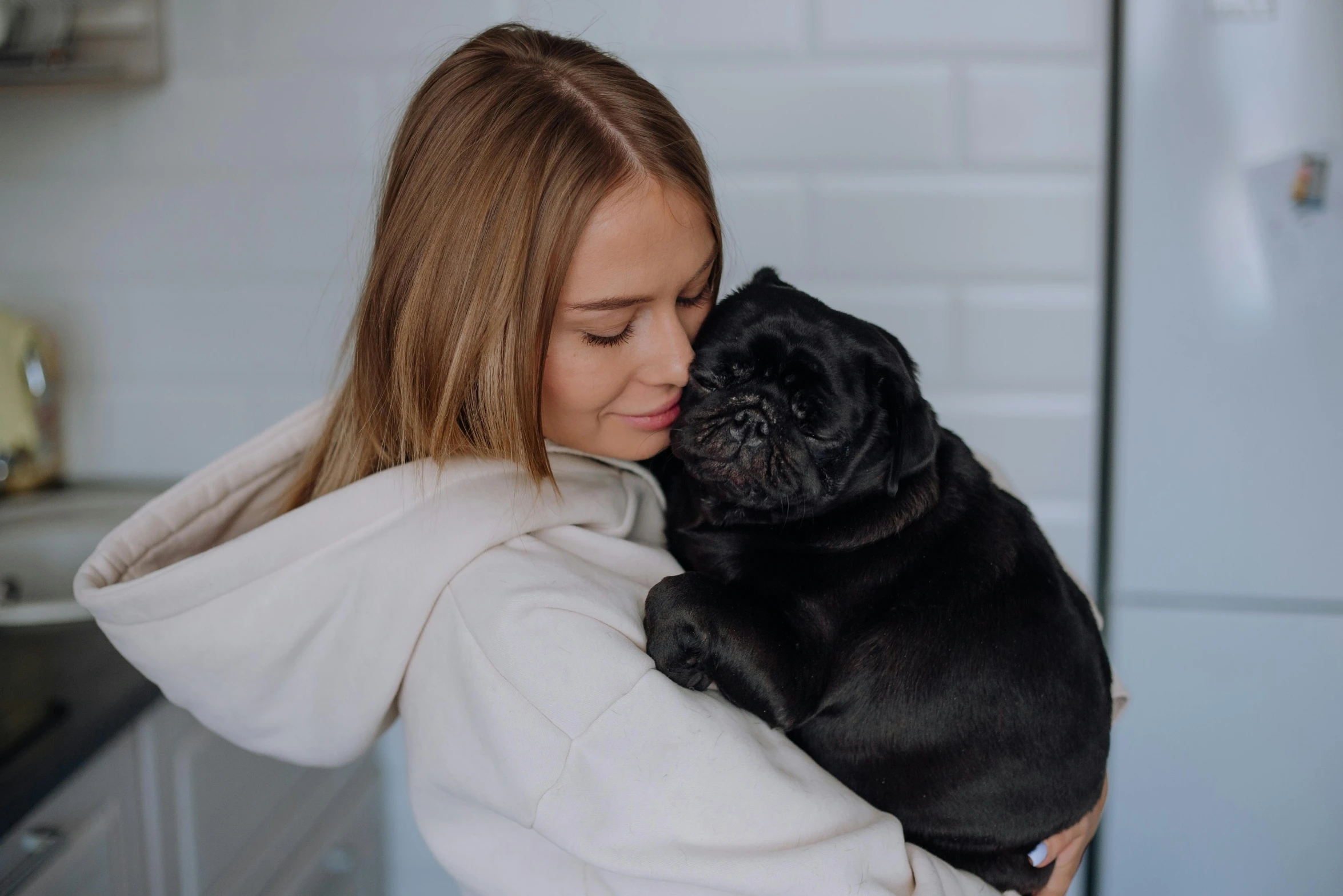 a woman in a white coat holding a black pug