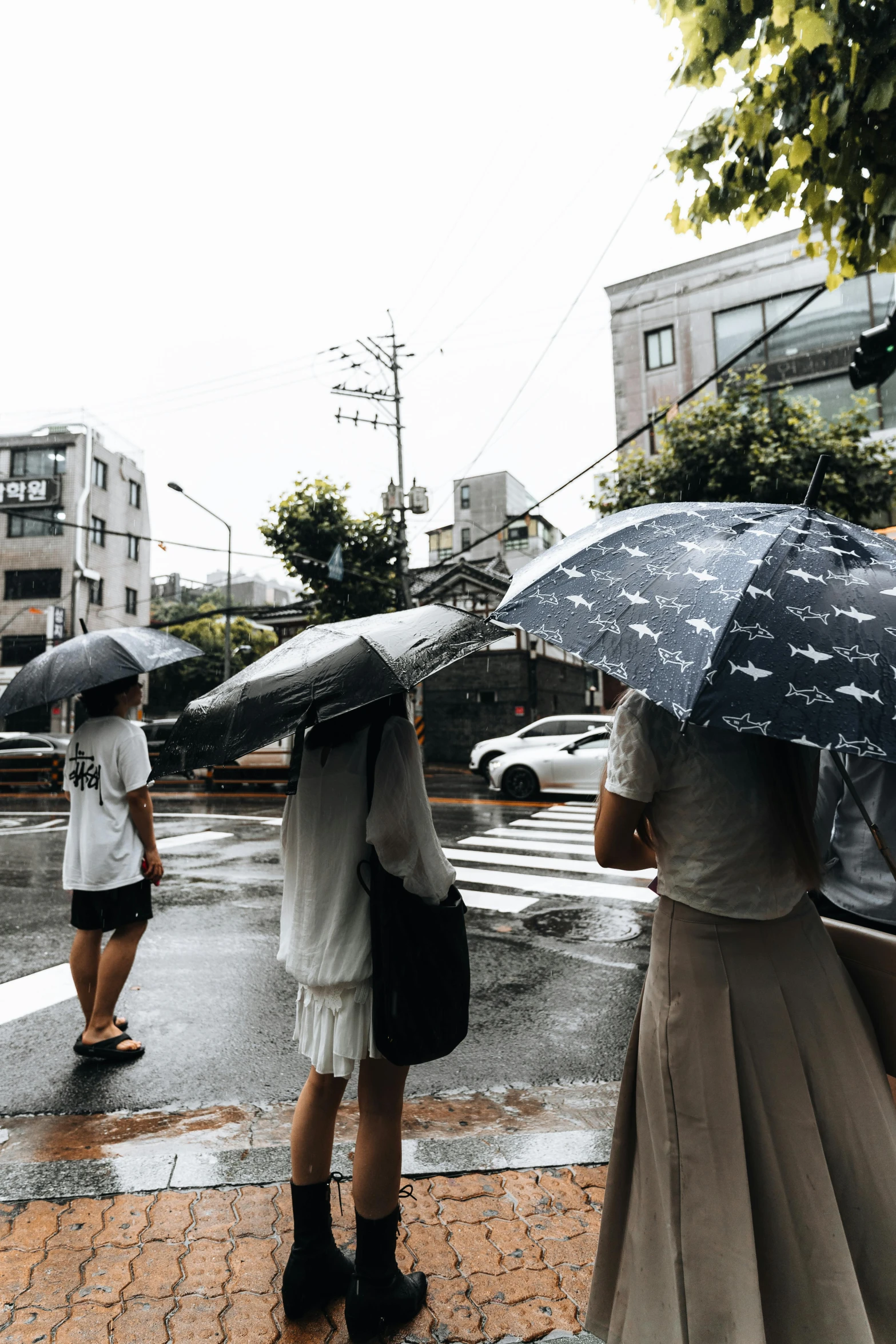 three people standing with umbrellas across a street