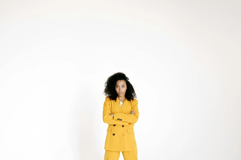 a woman dressed in a yellow ensemble stands against a white wall