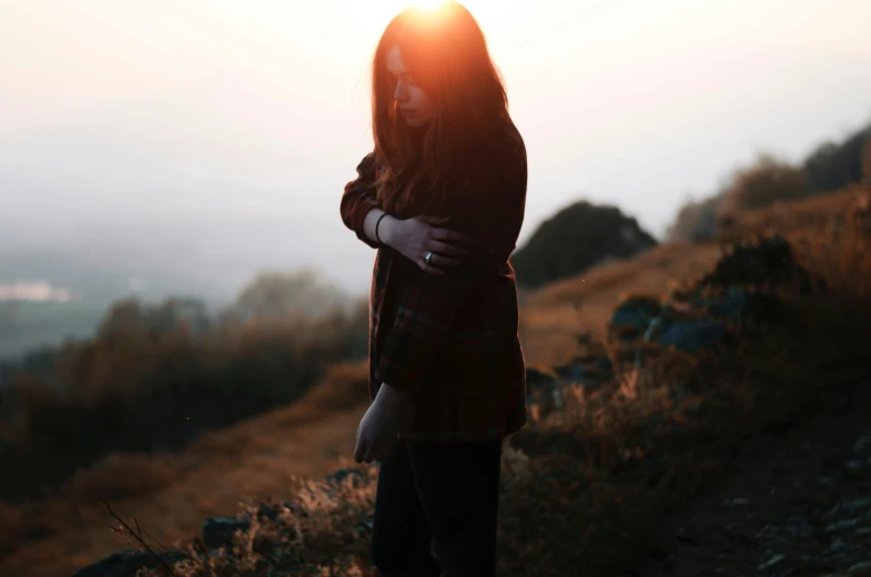 a girl stands on a hillside looking down at the sun