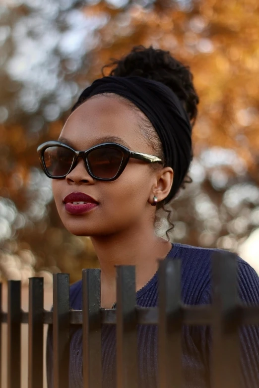 an african american woman with sunglasses and a top knot bun stands in front of the fence