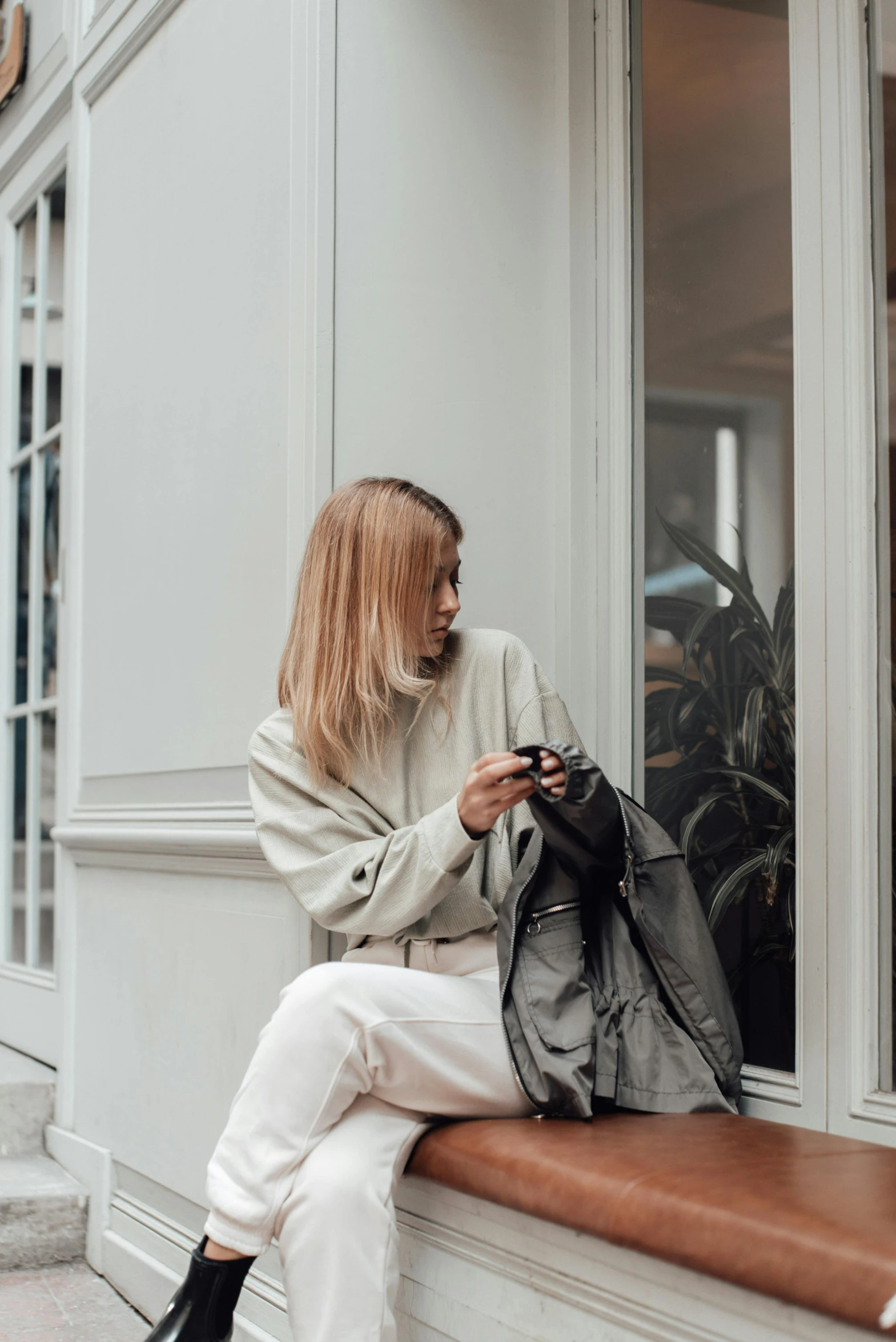 a young woman sitting on the window sill looking at her cellphone