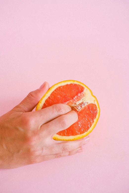 a person holding an orange fruit on a pink background