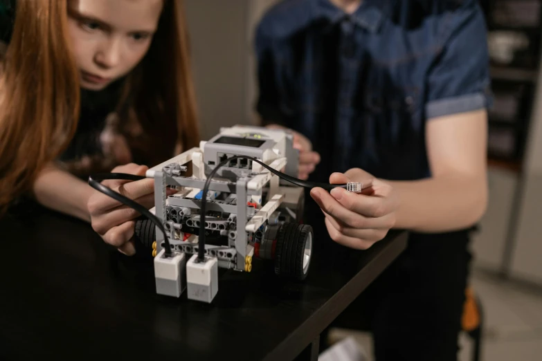 two girls assembling robot cars together with wires on the table