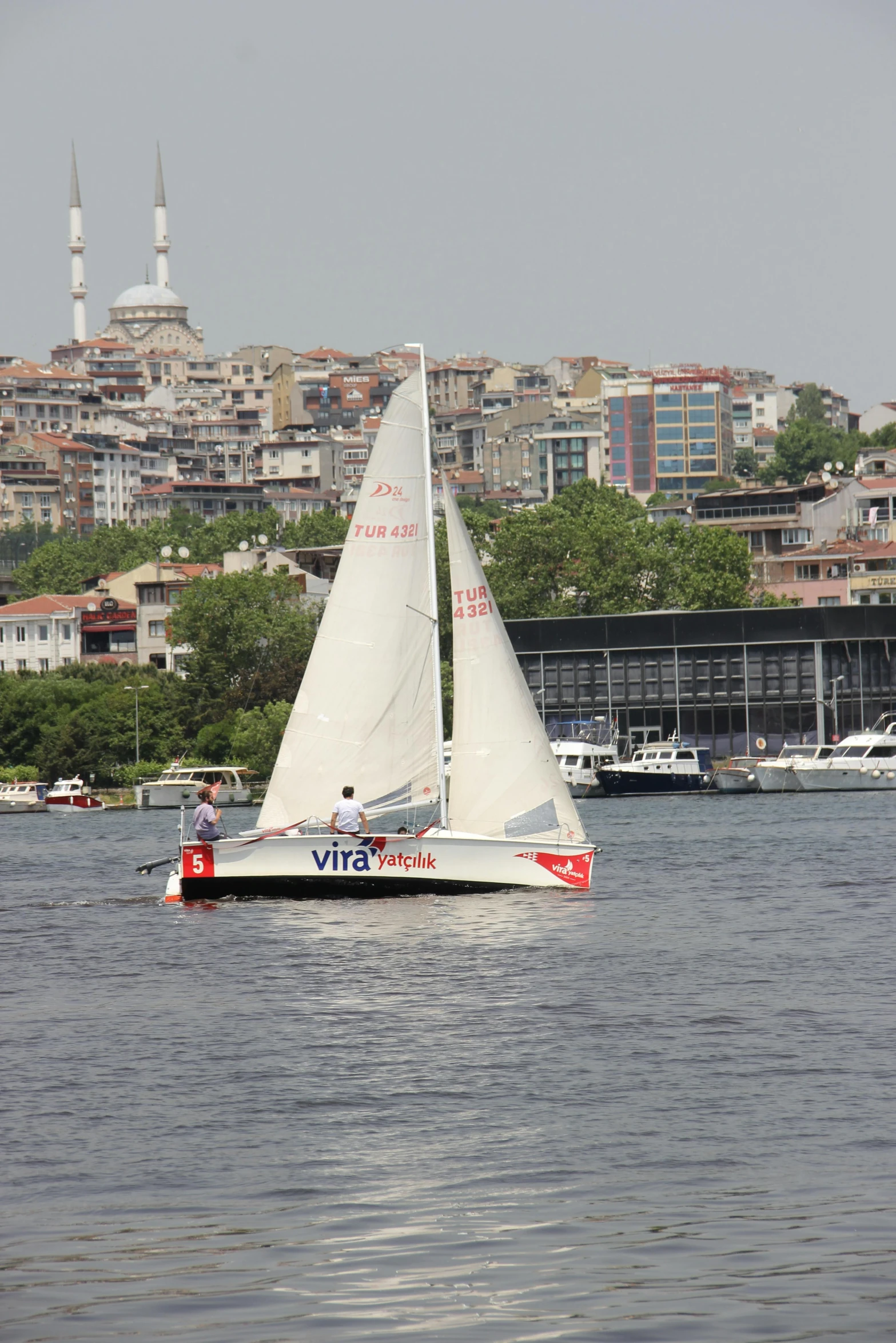 two men in a small sailboat in front of buildings on the water