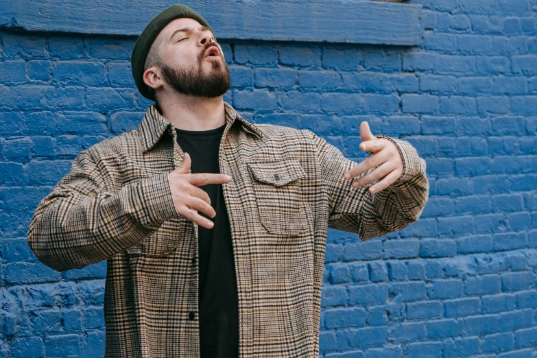 man with beard standing by blue wall with finger up