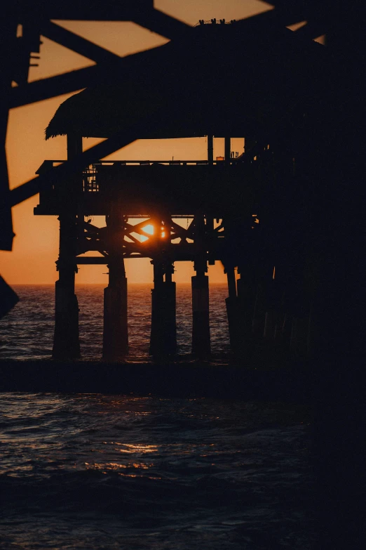 the sun setting over the water by a pier