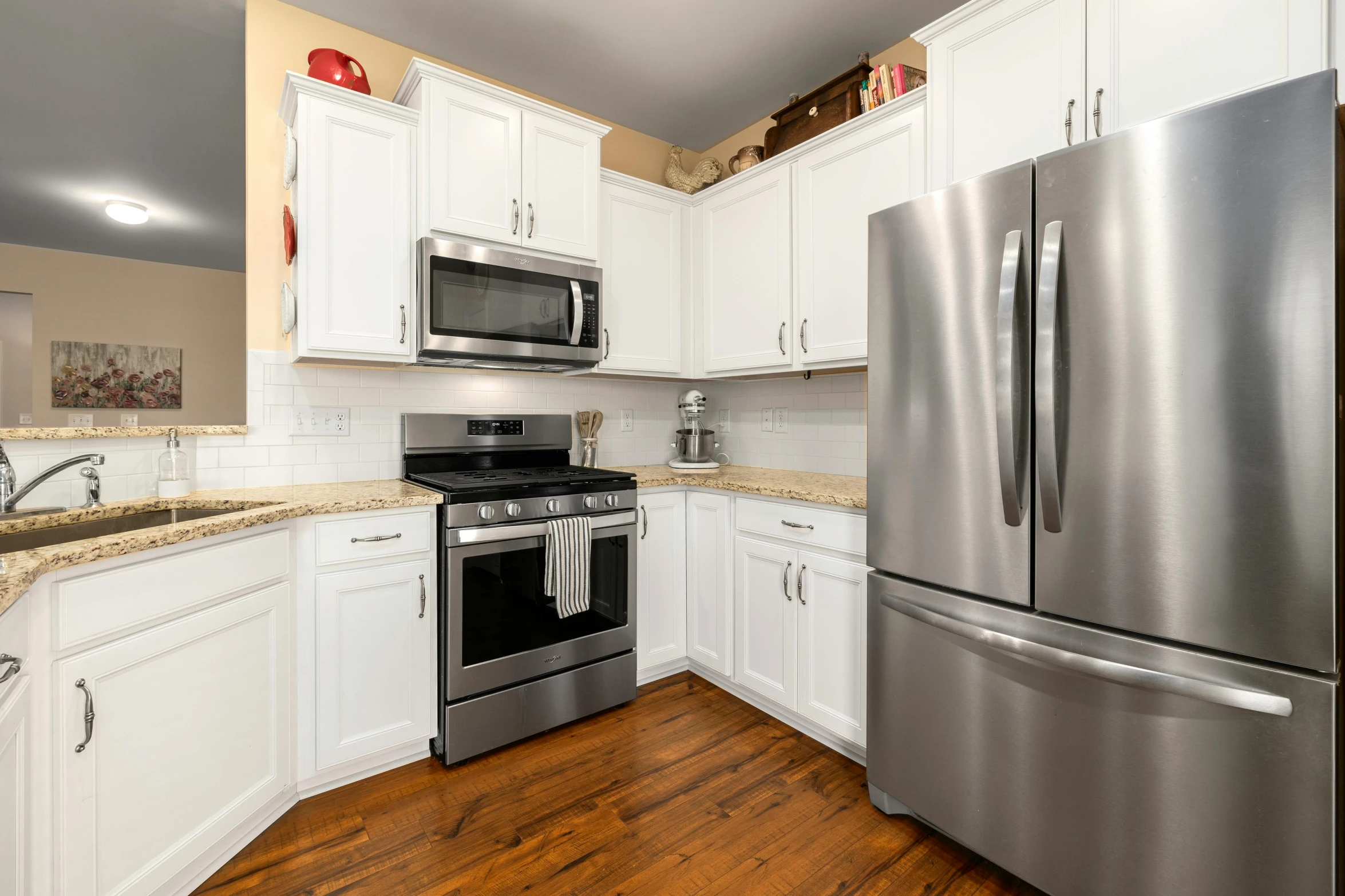 the kitchen has white cabinets, silver appliances and hard wood floors