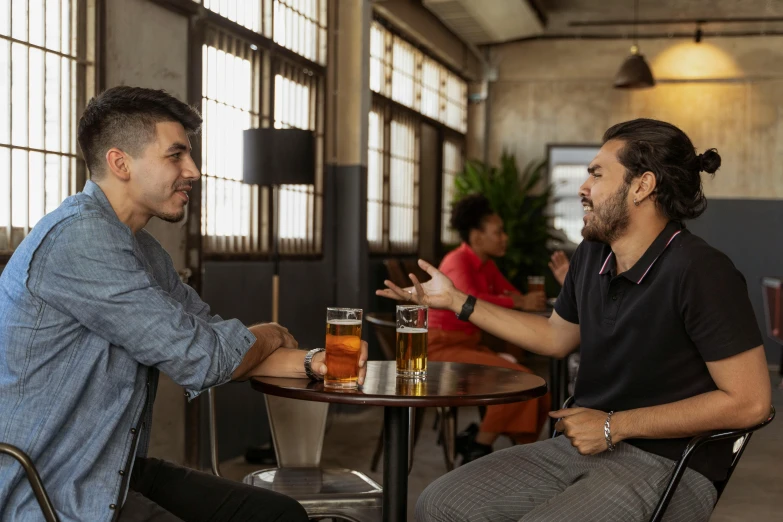 two people sit at tables talking and drinking