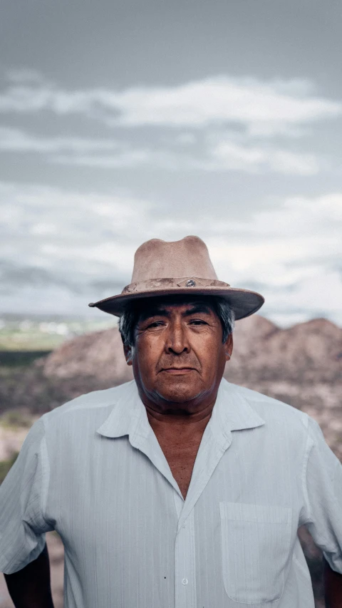 a man with hat and grey shirt standing next to hills