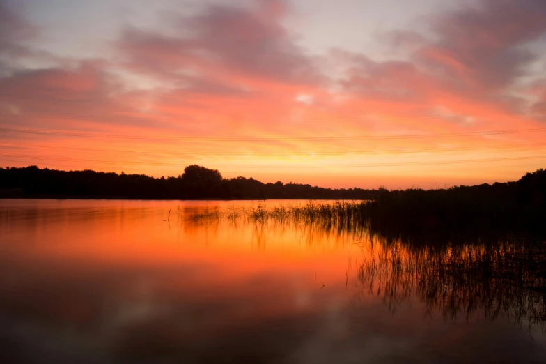 a body of water at sunset with red clouds and trees