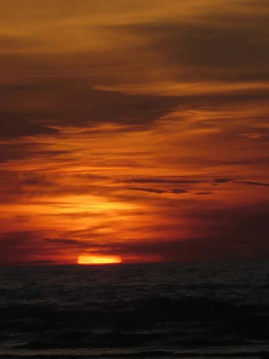 a lone plane flying over the ocean during sunset