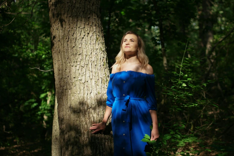 a woman in a blue dress poses near a tree