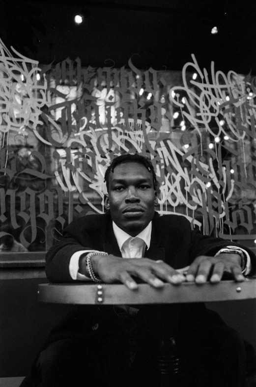 a black man sitting at a table in front of an illuminated wall