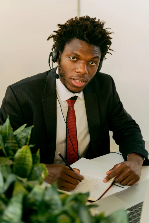 a young man wearing headphones, a suit and tie, writing in a book