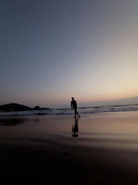 person walking on wet sand at low tide during sunset