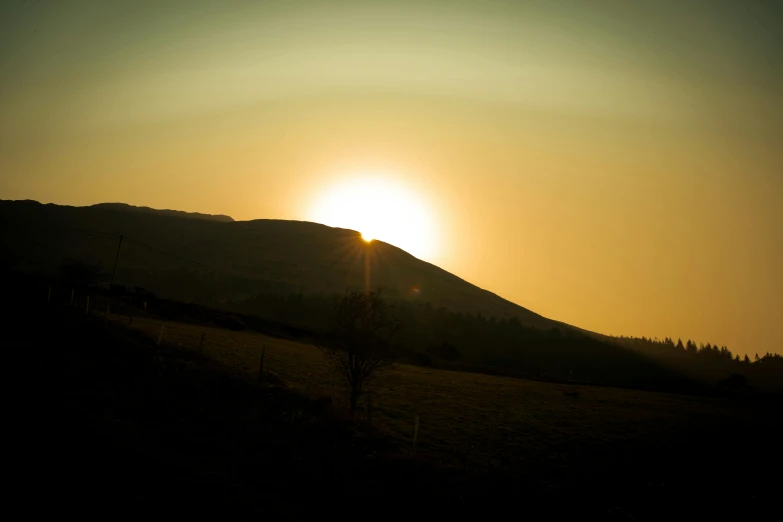 a sunset s of a field with trees and mountains