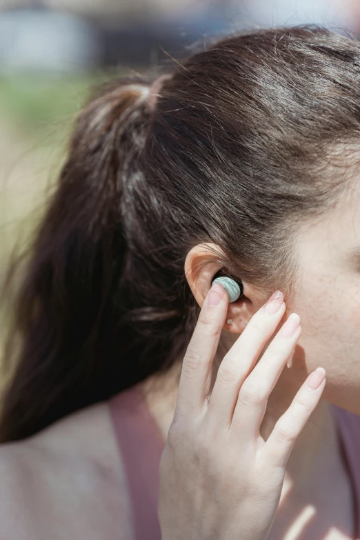 a woman with dark hair and earrings holds her ear