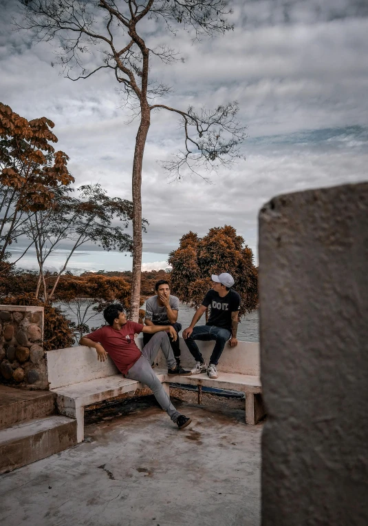 two young men sitting on benches by a tree