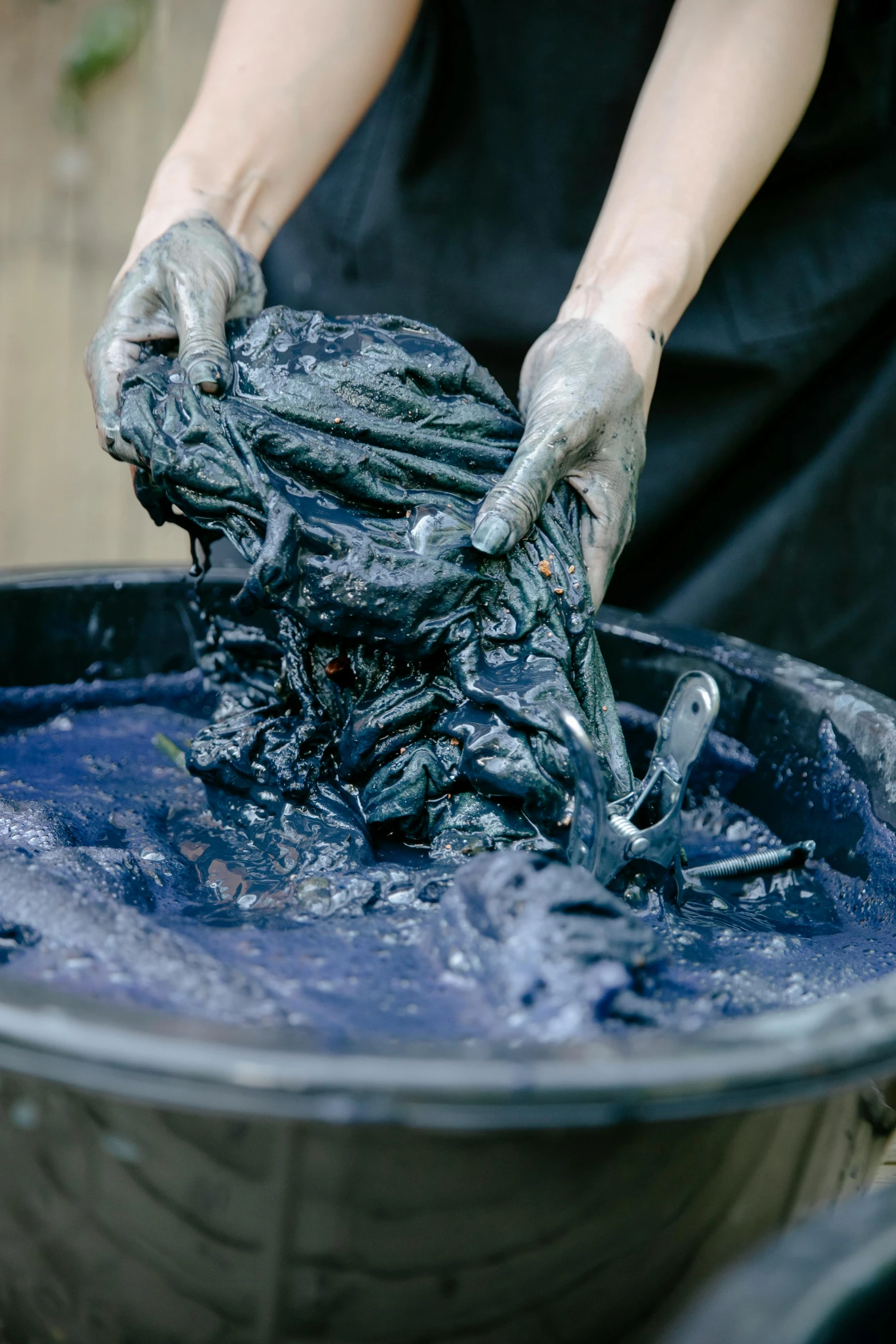 a bucket with a cloth covered in blue dye being washed by someone with white gloves