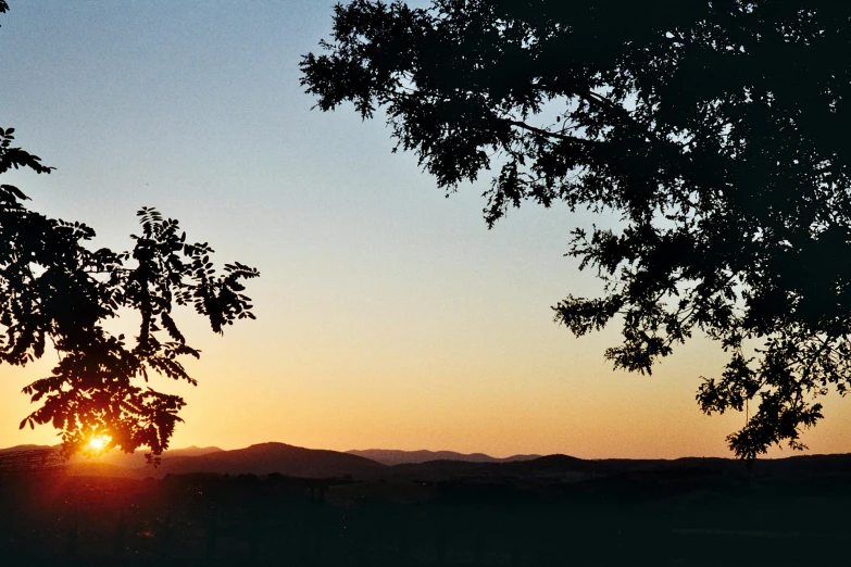 the sun is setting behind some trees and hills