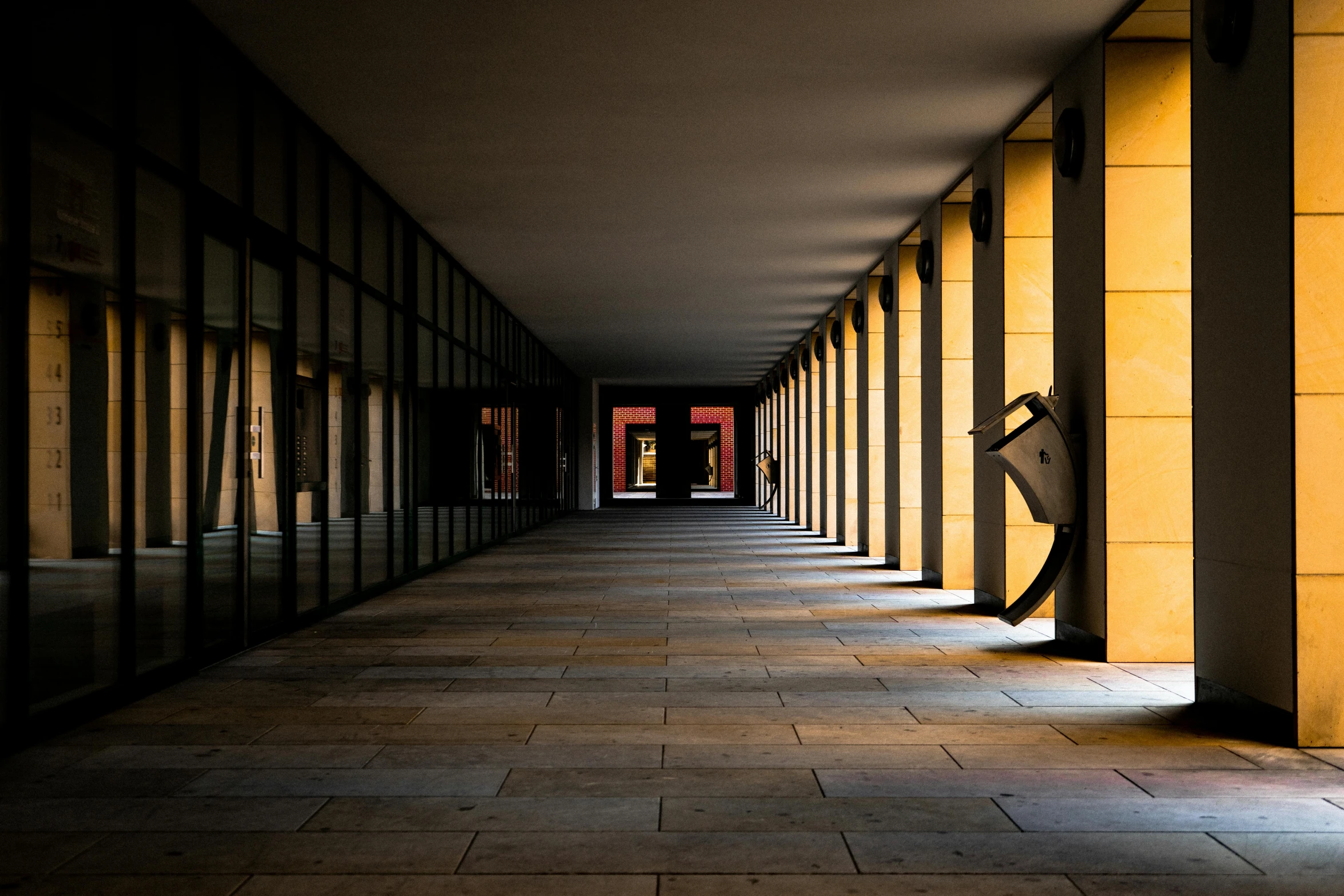 a long hallway leading to a yellow building with light shining in