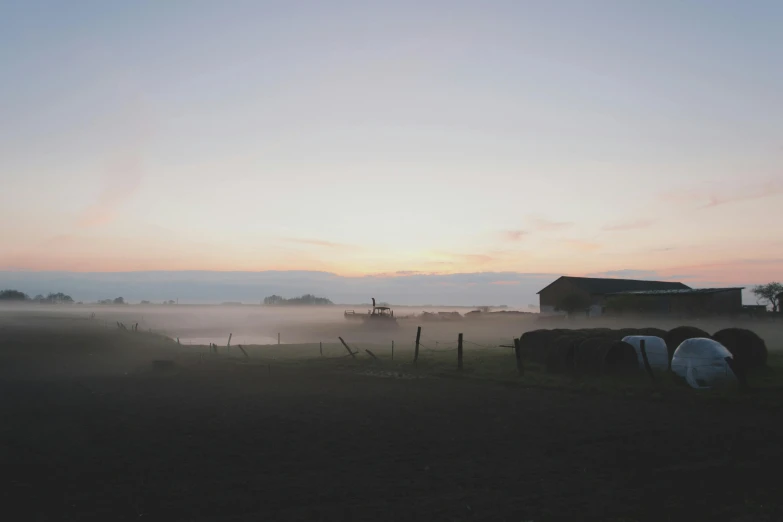 the sun is setting over hay bales near a barn