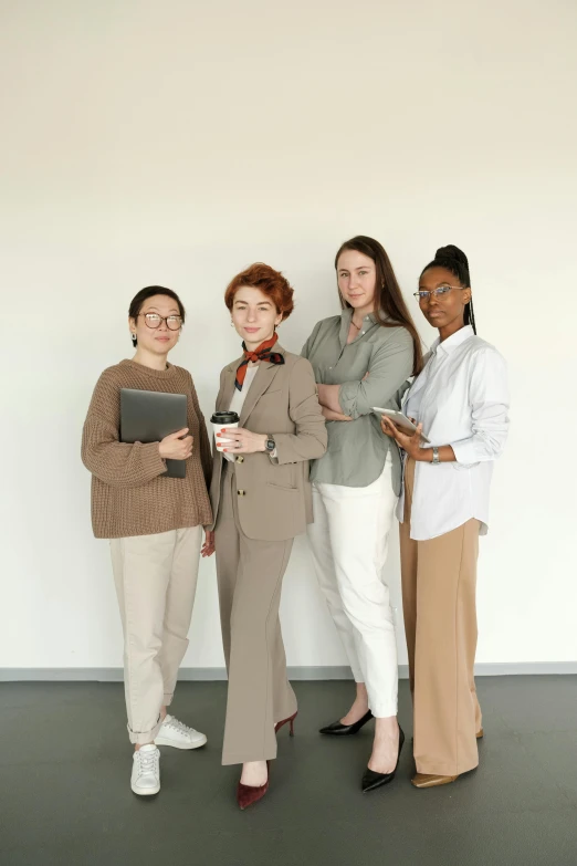 three females are posing for the camera in front of a white wall