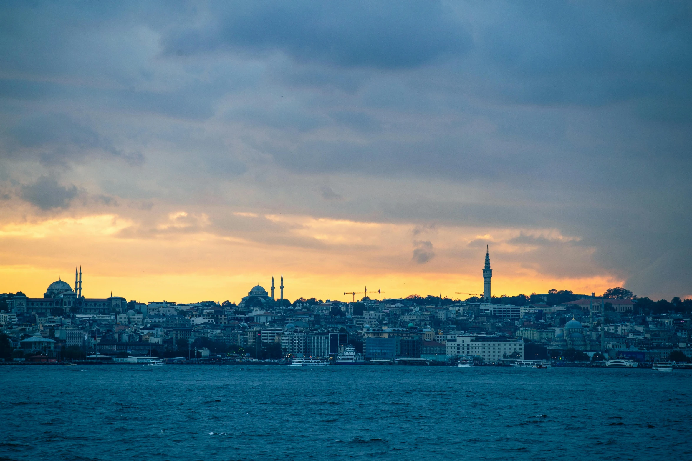 a sail boat sailing past a city under a dark cloudy sky