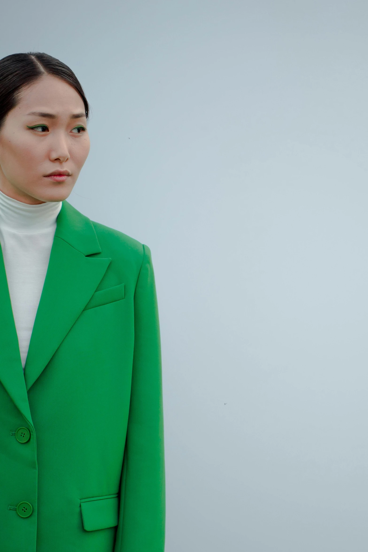 an asian woman in a green jacket stands