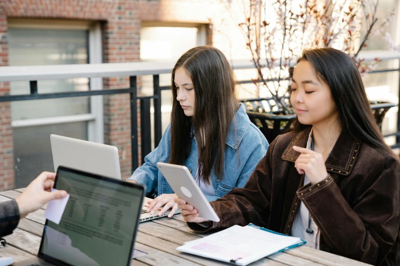 two young women sitting at a table while looking at soing on their laptop