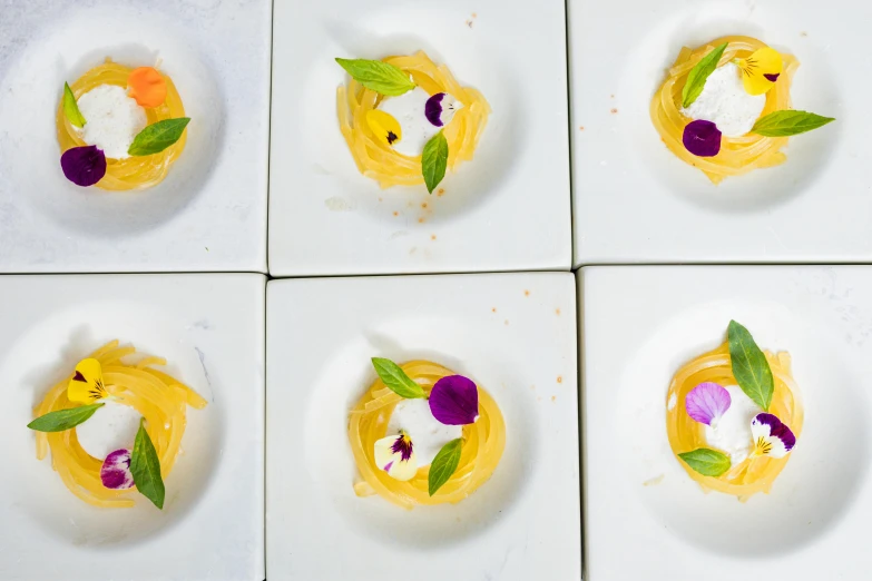 six square white plates with different pastries decorated with purple, yellow and green leaves