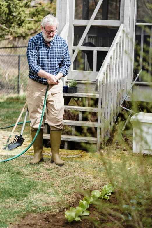 a man in a checkered shirt and brown pants holding a broom outside a house