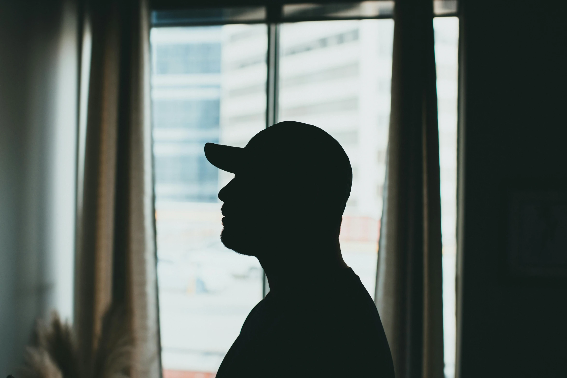 a man in silhouette wearing a hat and looking out a window