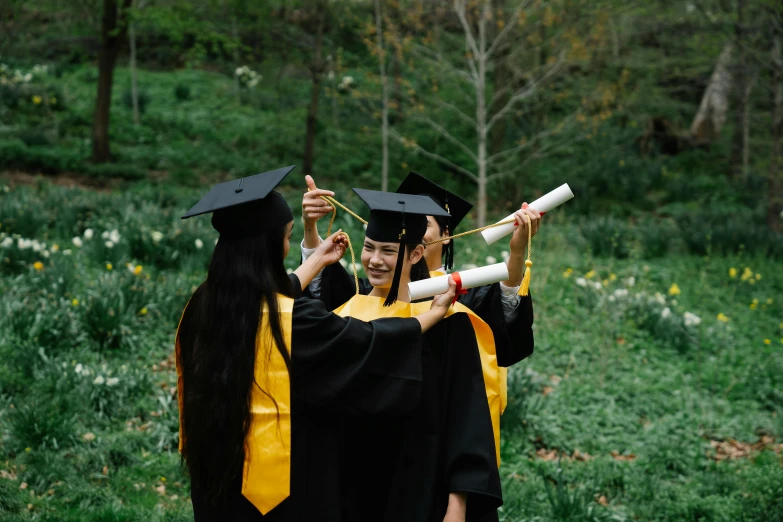 three graduates each hold their diplomas high in the forest