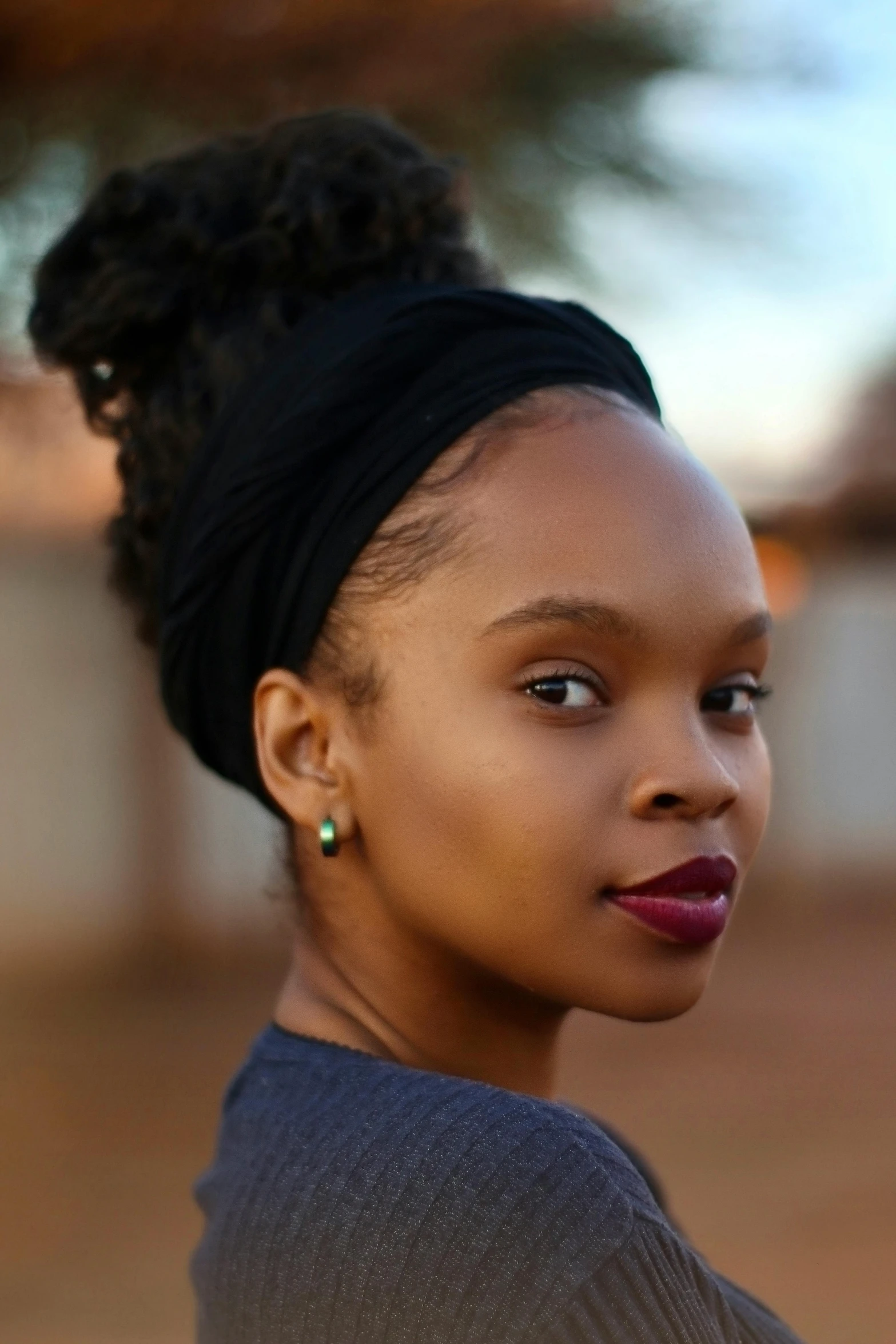 an african american woman wearing a dark dress with black hair, a top knot and earrings