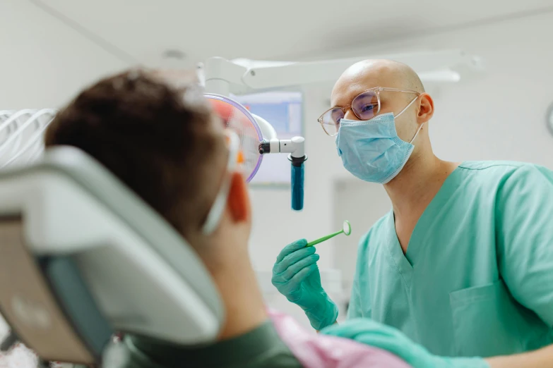 a dentist wearing glasses and mask talks to a patient