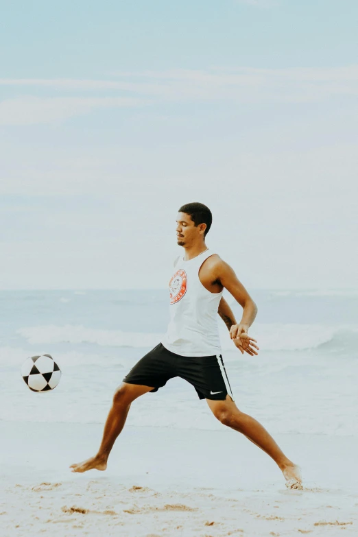 man kicking a ball on the beach, while another person watches